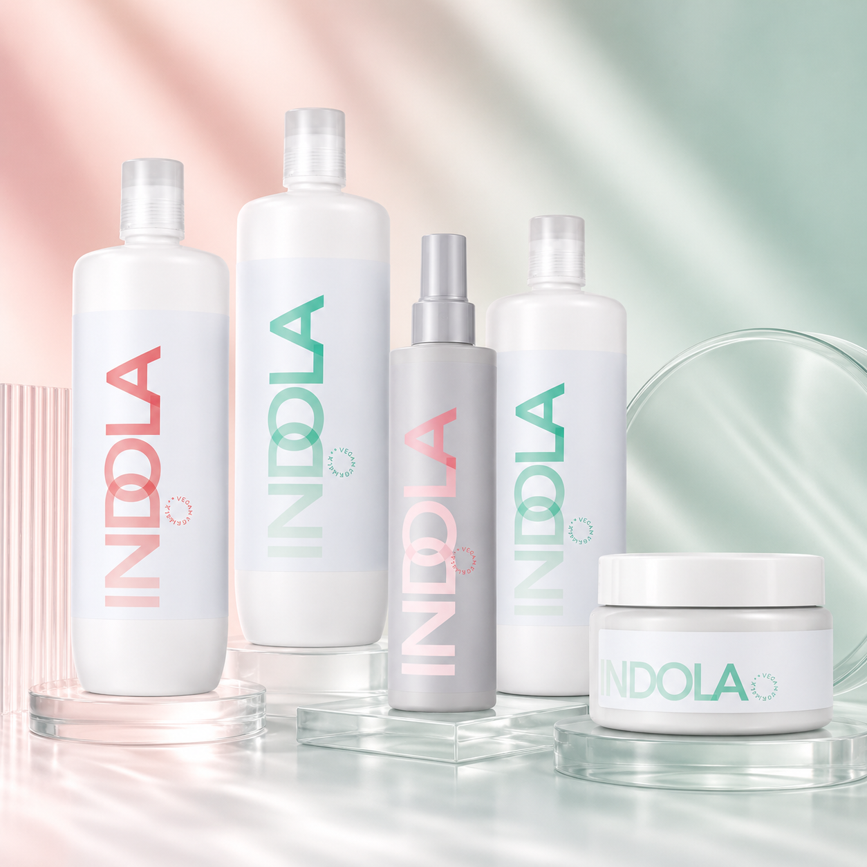 Selection of Indola shampoo, conditioner, treatment and thermal protection products displayed on a soft pastel pink and mint background with glass accents.