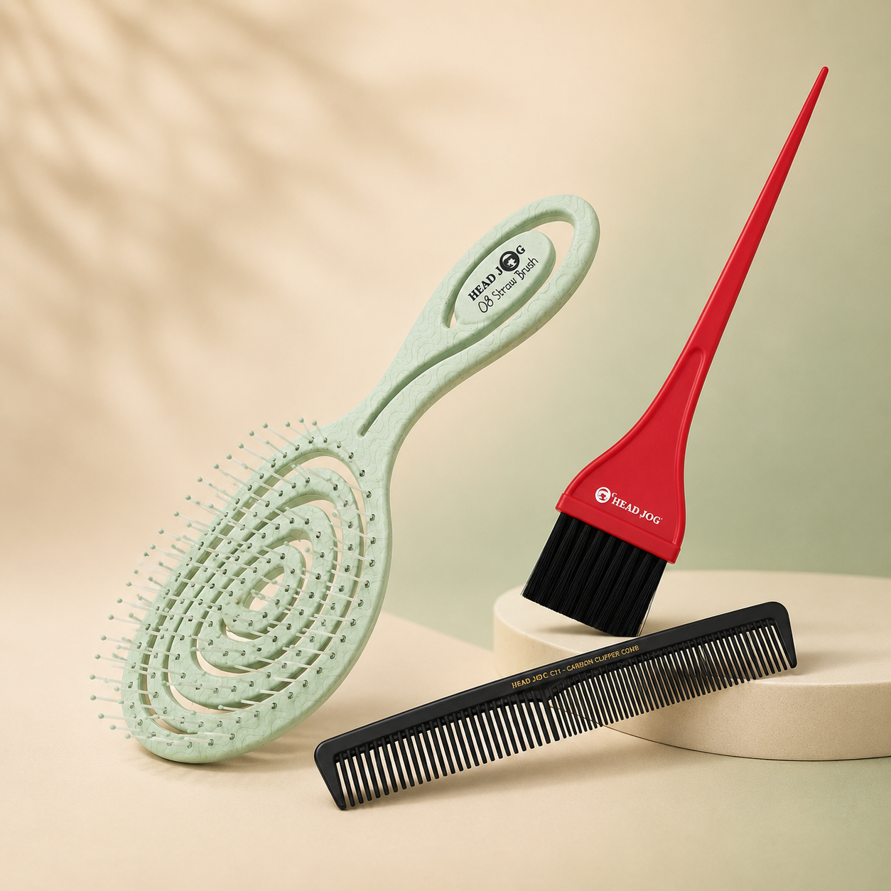 Premium collection image featuring a Head Jog Straw Brush, tint brush and carbon comb on a soft beige and sage gradient background with subtle natural shadows.